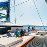 Small group of guests on a luxury catamaran bow in the Santorini caldera during a boat tour, Greece